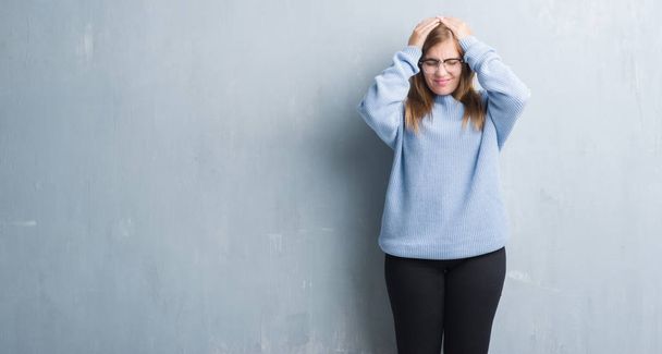 Mulher adulta jovem sobre parede grunge cinza usando óculos que sofrem de dor de cabeça desesperada e estressada porque dor e enxaqueca. Mãos na cabeça
. - Foto, Imagem