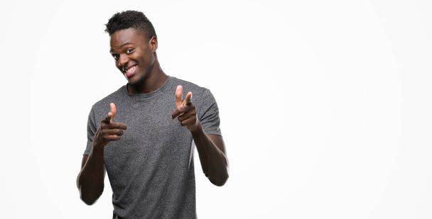 Nuori afrikkalainen amerikkalainen mies yllään harmaa t-paita osoittaa sormella kameraan iloinen ja hauska kasvot. Hyvä energia ja vibes
. - Valokuva, kuva