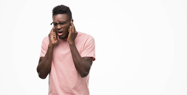 Młody człowiek african american sobie różowy t-shirt krycia uszy palcami z zirytowany wyrażenie dla hałasu głośno muzyki. Koncepcja głuchy. - Zdjęcie, obraz