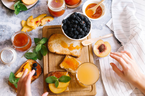 Tostadas de pan con mermelada de albaricoque y frutas frescas con hojas sobre mesa de madera blanca. Sabroso desayuno
. - Foto, Imagen