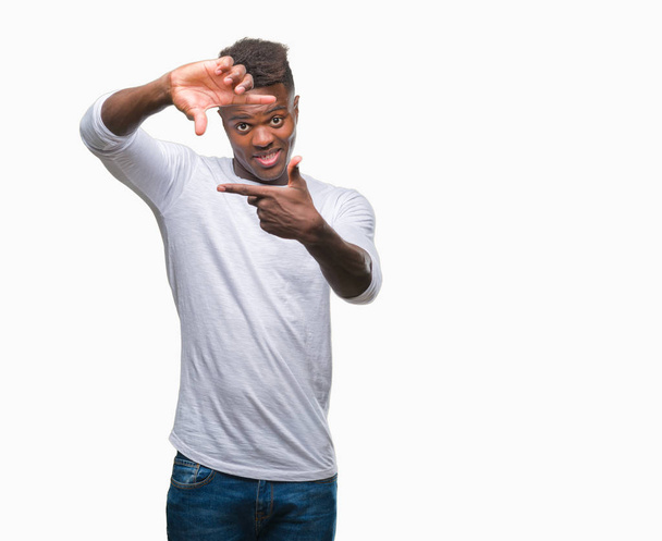 Jeune homme afro-américain sur fond isolé souriant faisant cadre avec les mains et les doigts avec le visage heureux. Concept de créativité et de photographie
. - Photo, image
