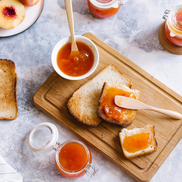 Tostadas de pan con mermelada de albaricoque y frutas frescas con hojas sobre mesa de madera blanca. Sabroso desayuno
. - Foto, Imagen