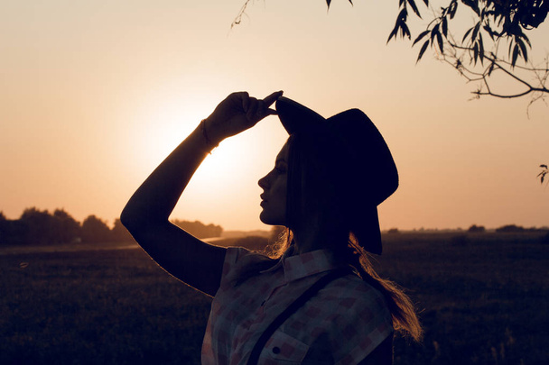 Une silhouette de femme touchant son chapeau regardant vers le bas
. - Photo, image