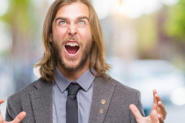 Young handsome business man with long hair over isolated background crazy and mad shouting and yelling with aggressive expression and arms raised. Frustration concept. - Photo, Image