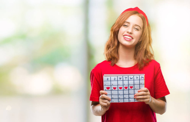 Young beautiful woman over isolated background holding menstruation calendar with a happy face standing and smiling with a confident smile showing teeth - Photo, Image