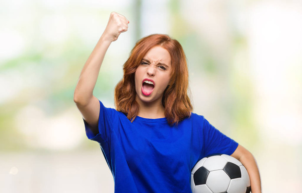 Jovem bela mulher sobre fundo isolado segurando bola de futebol irritado e frustrado gritando com raiva, louco e gritando com a mão levantada, conceito de raiva
 - Foto, Imagem