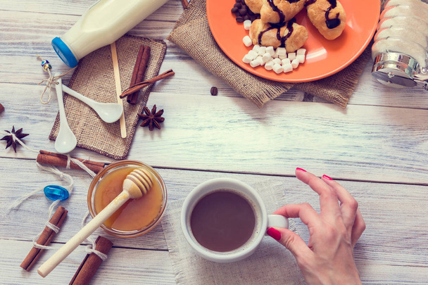 Female hand holds a cup of coffee in the background with croissants, honey  and milk - Foto, Bild