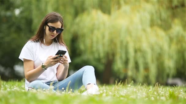 Femme mignonne lit le message texte sur le téléphone portable tout en étant assis dans le parc. - Séquence, vidéo