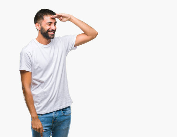 Hombre hispano adulto sobre fondo aislado muy feliz y sonriente mirando lejos con la mano sobre la cabeza. concepto de búsqueda
. - Foto, Imagen