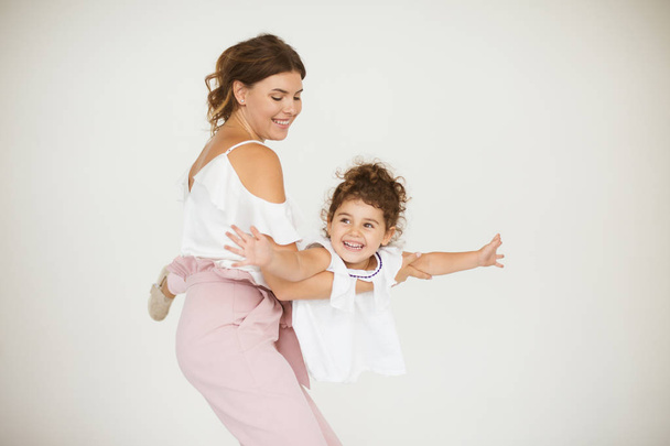Красивая улыбающаяся мать держит милая маленькая дочь счастливо играть в самолете полета вместе на белом фоне
 - Фото, изображение