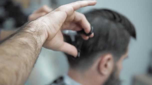 Close-up of barber cuts the hair by scissors at barbershop. Hairdressers hands at working process. Barber making haircut of attractive bearded man in barbershop. Hairdresser at work. Beauty saloon. - Filmmaterial, Video