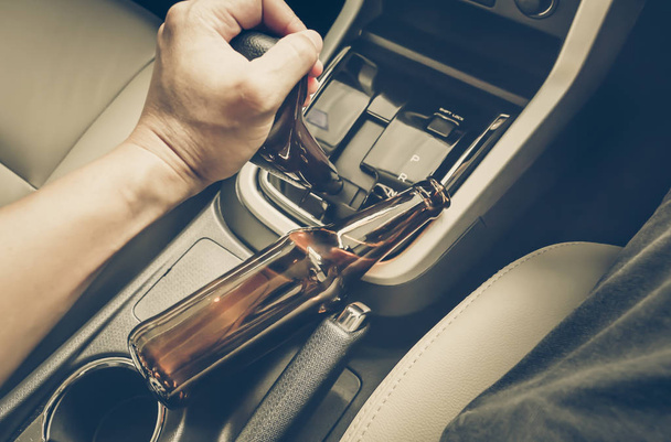 Un conductor sosteniendo una botella alcohólica mientras conduce / concepto de conducción ebria
 - Foto, Imagen