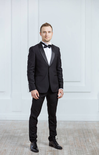 Attractive young man in tuxedo looking at camera indoors - Photo, Image