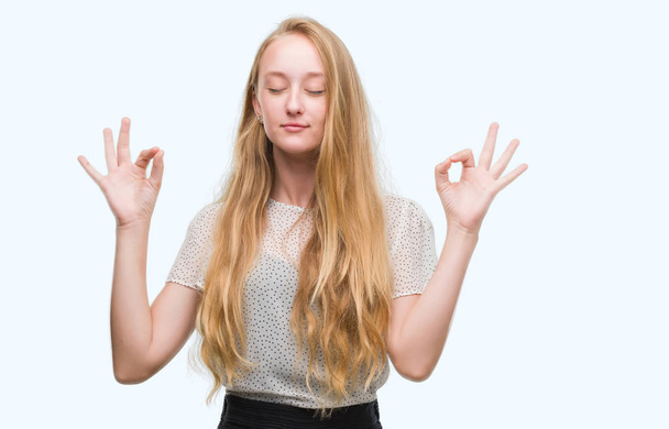 Blonde teenager woman wearing moles shirt relax and smiling with eyes closed doing meditation gesture with fingers. Yoga concept. - Photo, Image