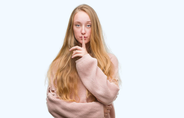 Dudaklarında parmak ile sessiz olmanı pembe kazak giymiş sarışın genç kadın. Sessizlik ve gizli kavramı. - Fotoğraf, Görsel