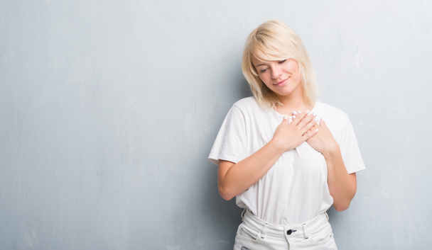 Adult caucasian woman over grunge grey wall smiling with hands on chest with closed eyes and grateful gesture on face. Health concept. - Photo, Image