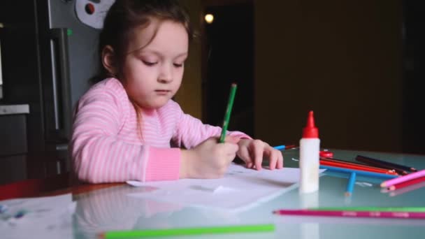 Adorable little Caucasian girl in pink sweater drawing shapes with a pencil on a sheet of paper, talking to someone. - Filmati, video