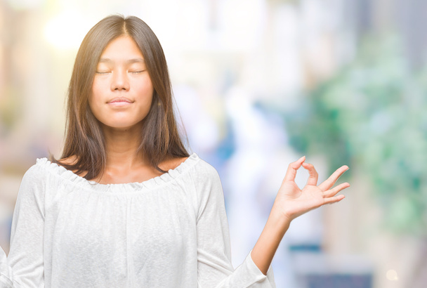 Jeune femme asiatique sur fond isolé se détendre et sourire les yeux fermés en faisant geste de méditation avec les doigts. Concept de yoga
. - Photo, image