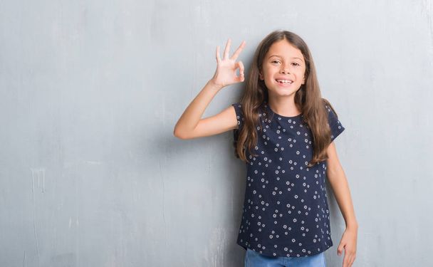 Young hispanic kid over grunge grey wall smiling positive doing ok sign with hand and fingers. Successful expression. - Foto, Bild