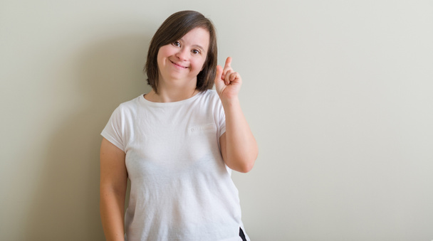 Frau mit Down-Syndrom steht über Mauer und zeigt mit erhobenem Zeigefinger auf erfolgreiche Idee. aufgeregt und glücklich. Nummer eins. - Foto, Bild