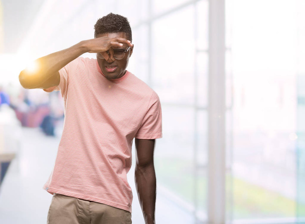 Jeune homme afro-américain portant un t-shirt rose sentant quelque chose de puant et dégoûtant, odeur intolérable, retenant son souffle avec les doigts sur le nez. Concept de mauvaises odeurs
. - Photo, image