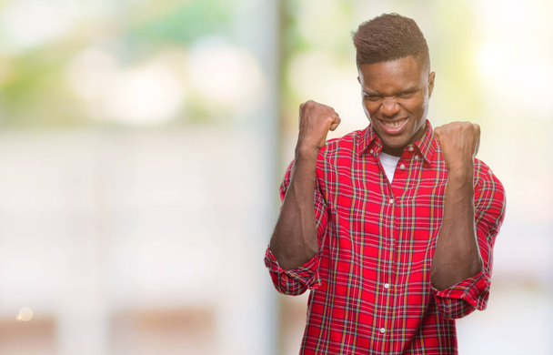 Hombre afroamericano joven sobre fondo aislado muy feliz y emocionado haciendo gesto ganador con los brazos levantados, sonriendo y gritando por el éxito. Concepto de celebración
. - Foto, Imagen