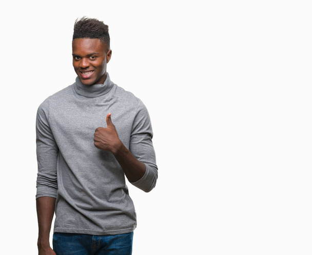 Jonge Afro-Amerikaanse man over geïsoleerde achtergrond gelukkig duimschroef opwaarts gebaar met de hand te doen. Goedkeuring van expressie kijken naar de camera met tonen van succes. - Foto, afbeelding