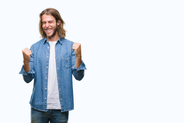 Young handsome man with long hair over isolated background very happy and excited doing winner gesture with arms raised, smiling and screaming for success. Celebration concept. - Photo, Image