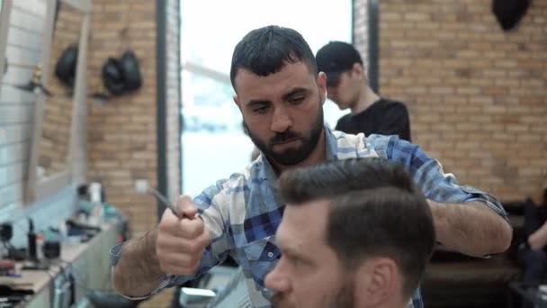 Close-up of barber cuts the hair by scissors at barbershop. Hairdressers hands at working process. Barber making haircut of attractive bearded man in barbershop. Hairdresser at work. Beauty saloon. - Záběry, video