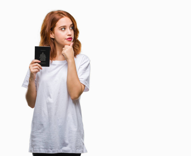 Молода красива жінка тримає паспорт канади над ізольованим тлом серйозне обличчя, думаючи про питання, дуже заплутана ідея
 - Фото, зображення