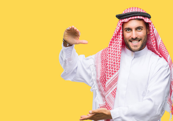 Jóképű fiatalember visel keffiyeh intett kezével mutatja a nagy és a nagy méretű jel, intézkedés szimbólum izolált háttérhez képest. Mosolyogva nézi a kamerát. Mérési koncepció. - Fotó, kép