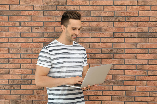 Man in casual clothes with laptop near brick wall - Photo, image