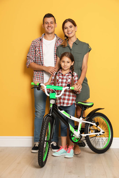 Portrait of parents and their daughter with bicycle near color wall - Фото, изображение