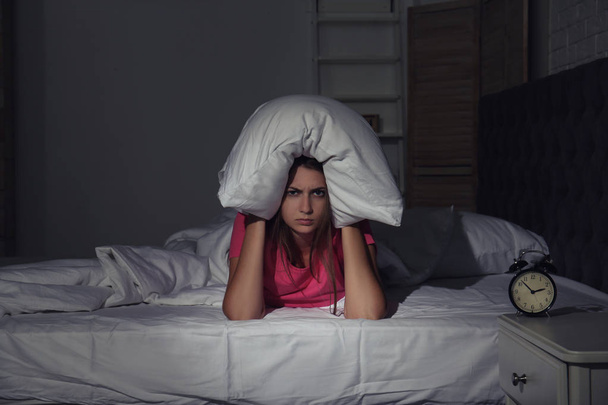 Молодая женщина покрывает голову подушкой в постели дома. Расстройство сна
 - Фото, изображение