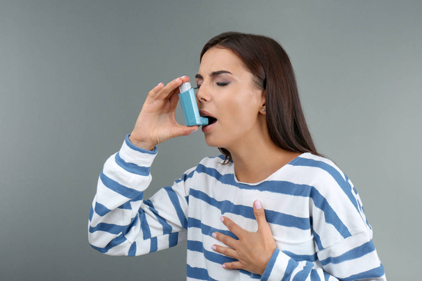Young woman using asthma inhaler on color background - Fotó, kép
