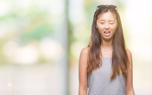Jovem mulher asiática usando óculos de sol sobre fundo isolado piscando olhando para a câmera com expressão sexy, rosto alegre e feliz
. - Foto, Imagem