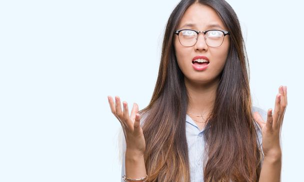 Mladých asijských obchodních žena nosí brýle nad izolované pozadí crazy a šílený křik a řvát s agresivní výraz a zvedl ruce. Frustrace koncept. - Fotografie, Obrázek