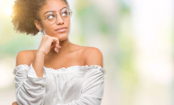Молодих афро-американської жінкою в окулярах над ізольованих фону з боку на підборіддя, думаючи про питання, замислений вираз. Усміхаючись з вдумливі обличчя. Сумніву концепції. - Фото, зображення