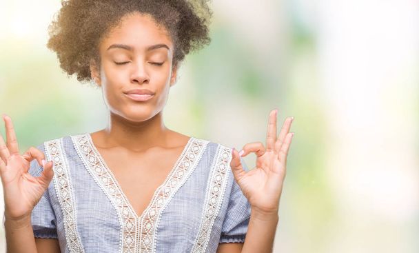Молодая афро-американка на изолированном фоне расслабляется и улыбается с закрытыми глазами, делая жест медитации пальцами. Концепция йоги
. - Фото, изображение