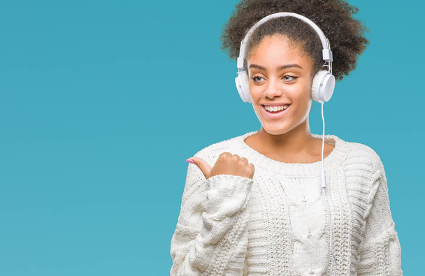 Young afro american woman wearing headphones over isolated background pointing and showing with thumb up to the side with happy face smiling - Foto, Imagem
