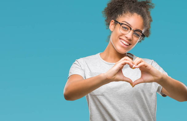 Mujer afroamericana joven con gafas sobre fondo aislado sonriendo en el amor mostrando el símbolo del corazón y la forma con las manos. Concepto romántico
. - Foto, imagen