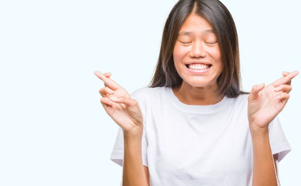 Jeune femme asiatique sur fond isolé souriant croisant les doigts avec espoir et les yeux fermés. La chance et le concept superstitieux
. - Photo, image