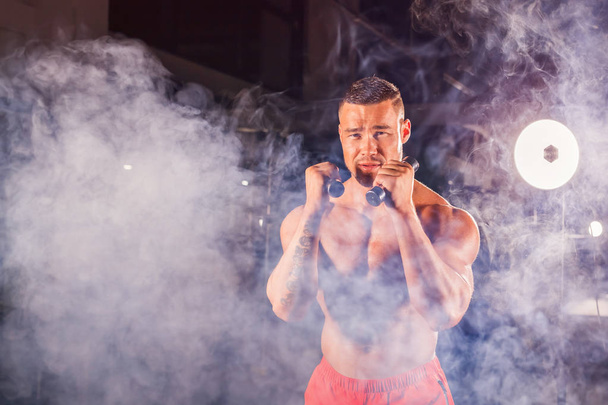 Kraftvoller Mann bei Boxübungen, Volltreffer mit Hanteln. Foto des sportlichen, muskulösen Rüden. Stärke und Motivation - Foto, Bild