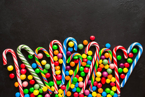 Candy canes with colorful drops on black background with copy space, flat lay - Foto, afbeelding