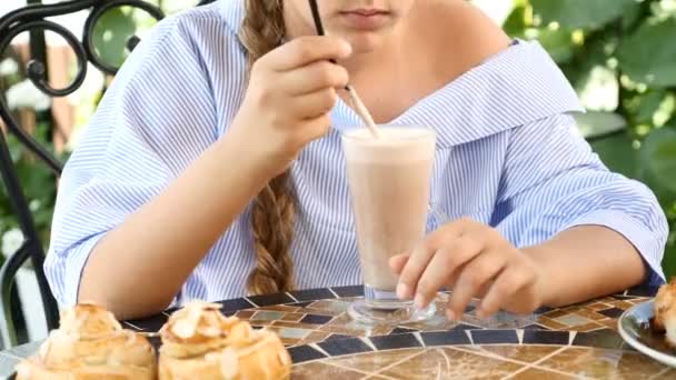 Elämäntapakäsite. Tunnistamaton kaunis tyttö nauttii cappuccino kahvilassa nuolee vaahtoa olki. Hyvää huomenta käsite
. - Materiaali, video