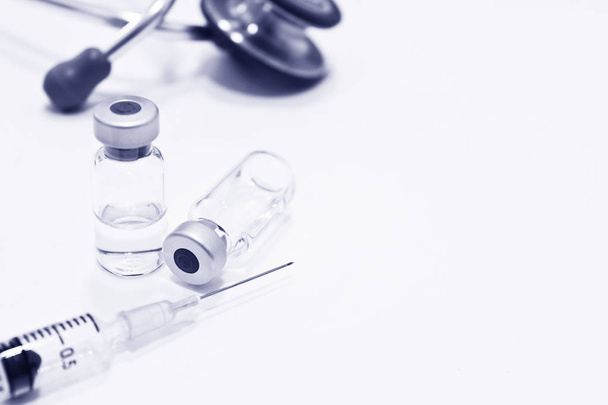 Injektiopullo lääkettä tai rokotetta, 3 ml muovinen ruisku neulalla ja epätarkka stetoskooppi eristetty valkoisella pohjalla, sininen sävy
 - Valokuva, kuva