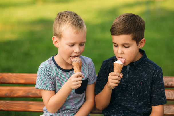 Los niños están sentados en el banco y comiendo helado.
 - Foto, Imagen