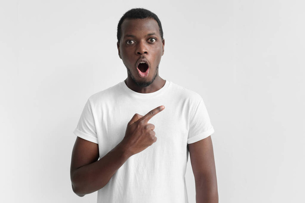 Emotional african american man isolated on gray background drawing attention to right side with shocked face, advertising something - Φωτογραφία, εικόνα