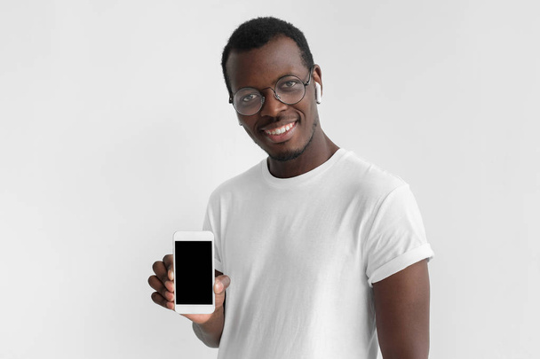 Young afrcian american man smiling isolated on gray background, holding and showing vertical blank smartphone with copyspace for advertisement of app or website - Foto, immagini