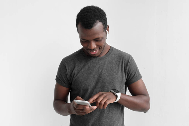 Young african american dark skin man looking at smartphone while texting, using mobile phone, isolated on gray background - Foto, imagen